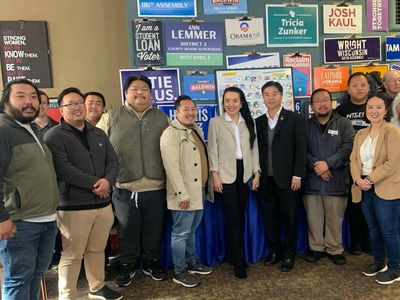 A diverse group of people stand smiling in front of a wall of political campaign signs.