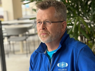 Man in blue Felaris sweater working with laptop and phone.