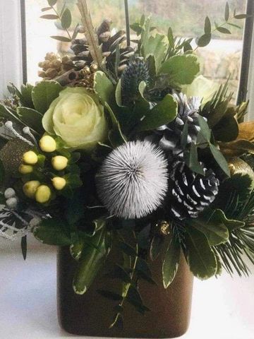A pot full of Christmas flowers with roses, carnations, fircones and spruce.