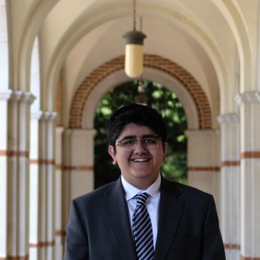 Young man in a suit smiling under an arched corridor.
