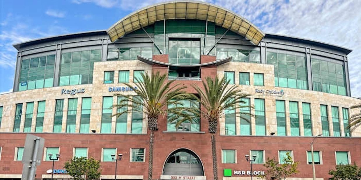 Modern commercial building with palm trees and multiple business signs.