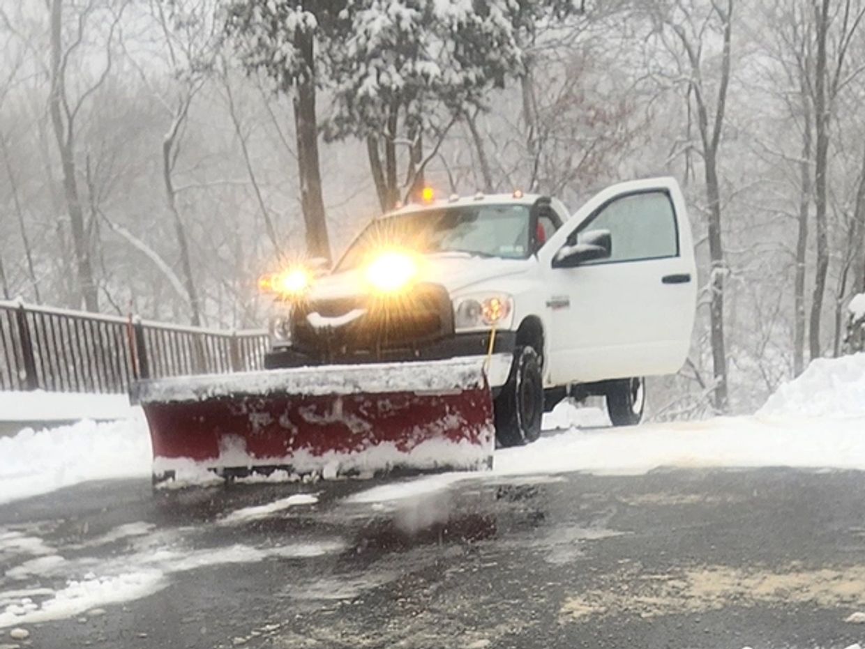 White truck with snow plow clearing snow on a winter road.