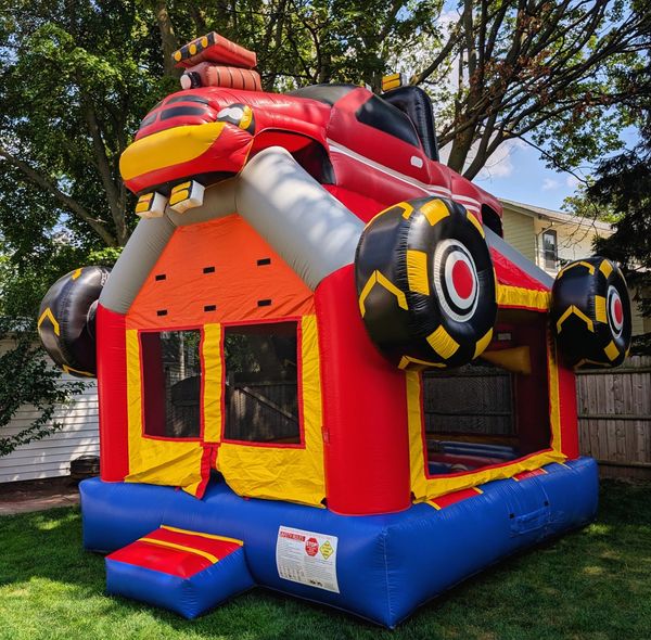 Colorful inflatable bounce house shaped like a monster truck in a backyard.