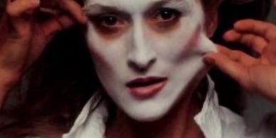 Person wearing a white theatrical mask and pulling it away from their face.