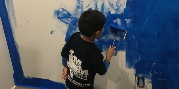 A child painting a wall blue with a paint roller.