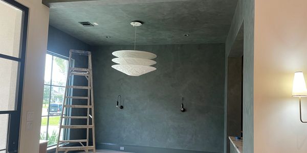 Empty room with textured walls, a ladder, and modern light fixtures.
