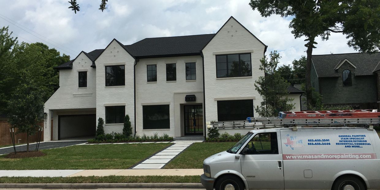 Modern white two-story house with black roof and large windows, a painting service van in front.