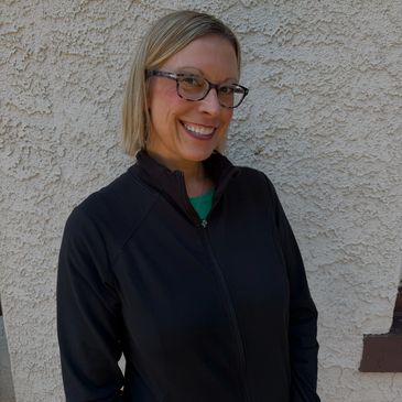 Smiling woman with glasses against textured wall.