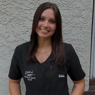 Smiling woman in a salon uniform standing against a grey wall.
