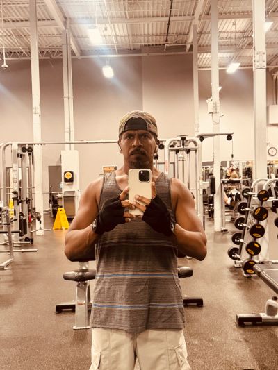 Man taking gym selfie wearing a tank top and gloves.