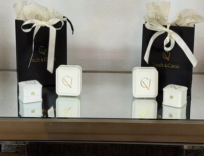 Two elegant black gift bags with white ribbons, each accompanied by white jewelry boxes on a reflective surface.