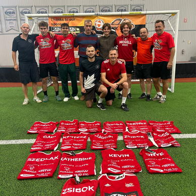 A group of men posing behind a soccer goal with red jerseys laid out in front.