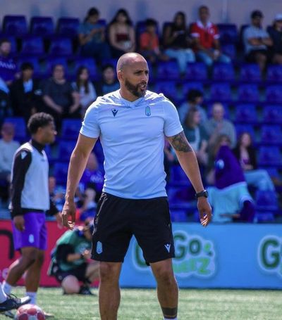 Man in sportswear standing on a soccer field with spectators behind.