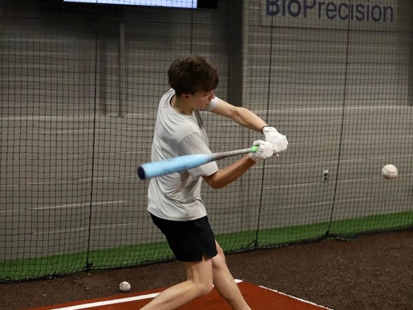 Young man swinging a baseball bat indoors at a batting cage.