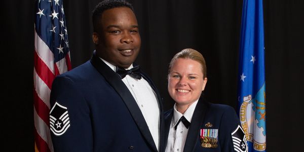 Two military personnel in dress uniforms smiling.