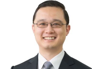 戴眼镜的亚洲男性，穿着西装和领带，微笑着。