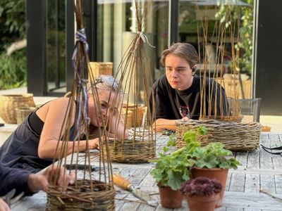 Two women focused on basket weaving at an outdoor wooden table.