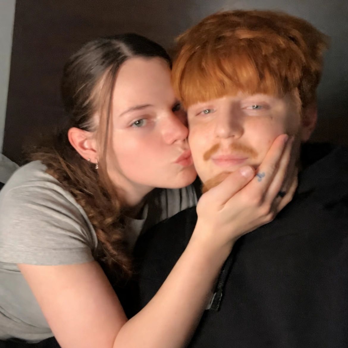 A woman kisses a man on the cheek, showing affection.