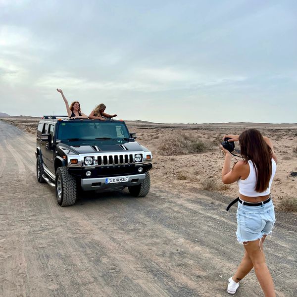 Dos chicas en una camioneta en el desierto mientras otra chica toma una foto de las mismas