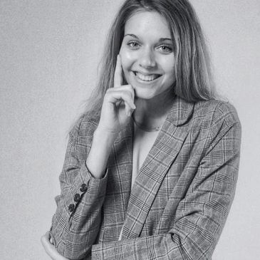 Young woman smiling, wearing a plaid blazer, posing with hand near face.