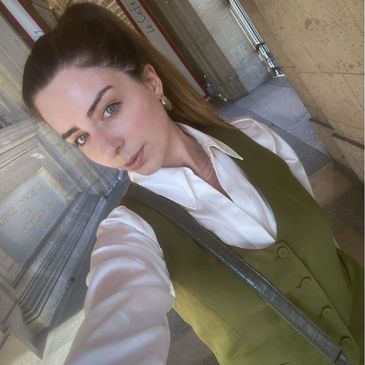 Woman wearing a white shirt and green vest taking a selfie outdoors.