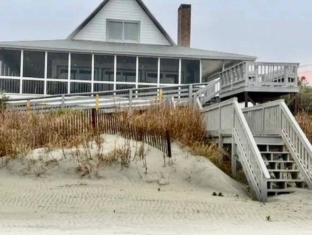 Beach house with wooden stairs and ramp leading to sand.
