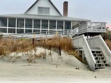 Beach house with wooden stairs and ramp leading to sand.