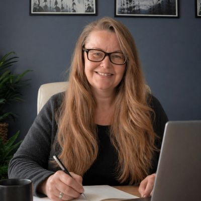 Smiling woman with glasses writing at a desk with a laptop.