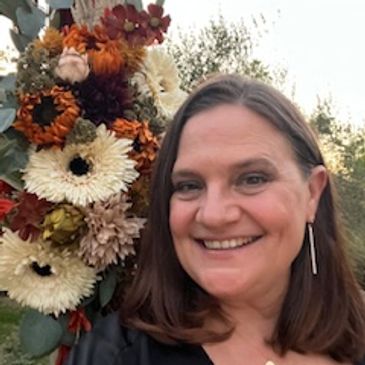 Woman smiling with autumn flowers in the background.