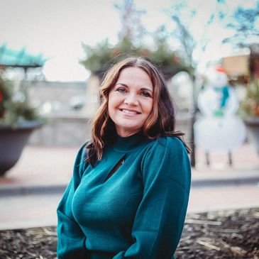 A woman smiling outdoors in a teal sweater.
