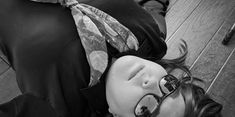 .Person with red hair wearing sunglasses and a colorful scarf lies on wooden floor