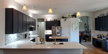 Modern kitchen with dark cabinets, white countertops, and a wooden floor under renovation.