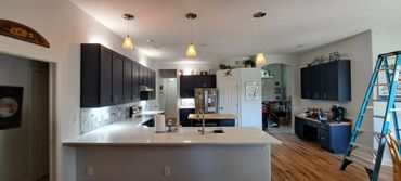 Modern kitchen with dark cabinets, white countertops, and a wooden floor under renovation.
