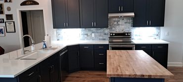 Modern kitchen with dark cabinets, white countertops, and a wooden island.