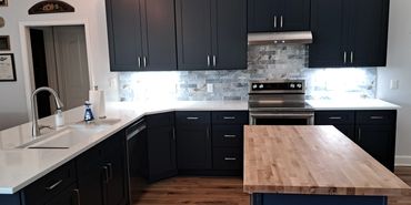 Modern kitchen with dark cabinets, white countertops, and a wooden island.