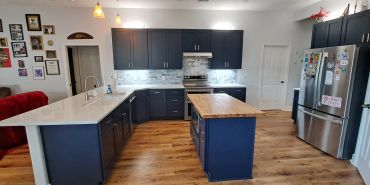 Modern kitchen with navy blue cabinets and wooden flooring.