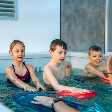 Children learning to swim with kickboards under instructor supervision in a pool.