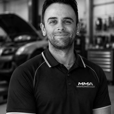 Smiling mechanic in a workshop wearing MMA polo shirt.
