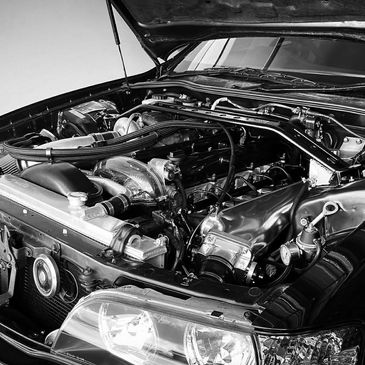 Black and white photo of a car engine bay with hood open.