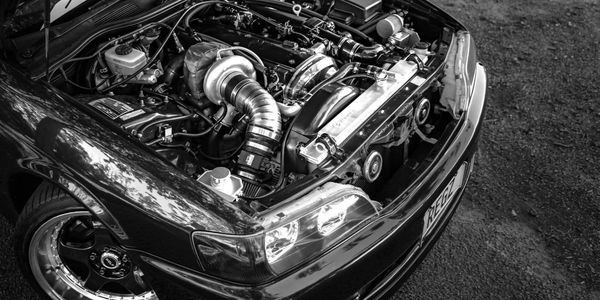 Black and white image of a car engine with hood open.