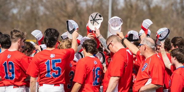 Baseball team raising hats in unison during a gathering.