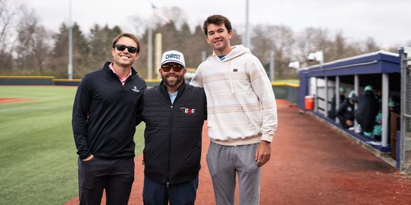 Three men smiling on a baseball field.
