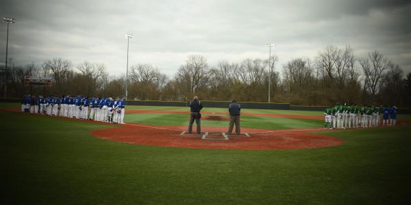 Two baseball teams lined up before a game with umpires at home plate.