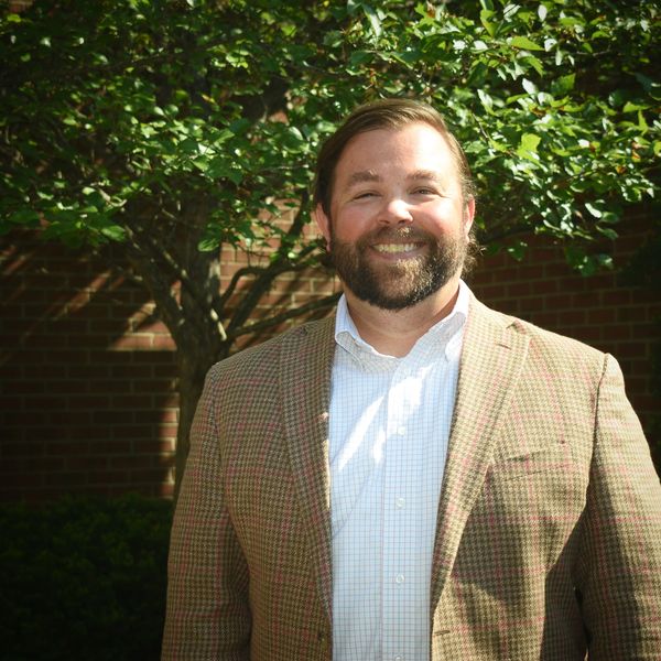 Smiling man in a blazer outdoors.