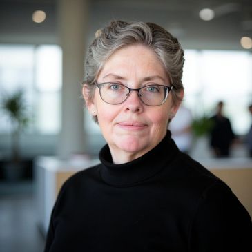 Photo of fair-toned mature woman wearing glasses in a black blouse in an office environment.