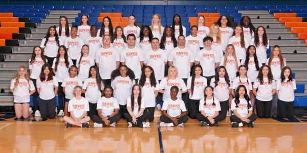 A large group of students posing in a gym wearing white "Hawks" shirts.