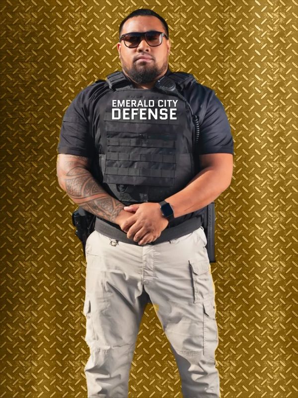 A man in black shirt and sunglasses standing on brown background.