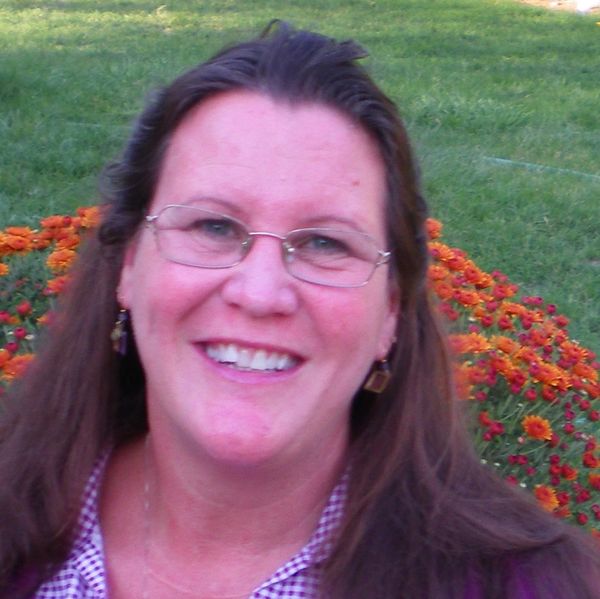 Smiling woman with glasses outdoors near flowers and grass.