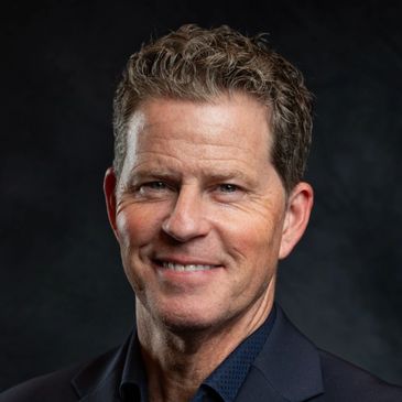 Smiling man in dark suit against a black background.