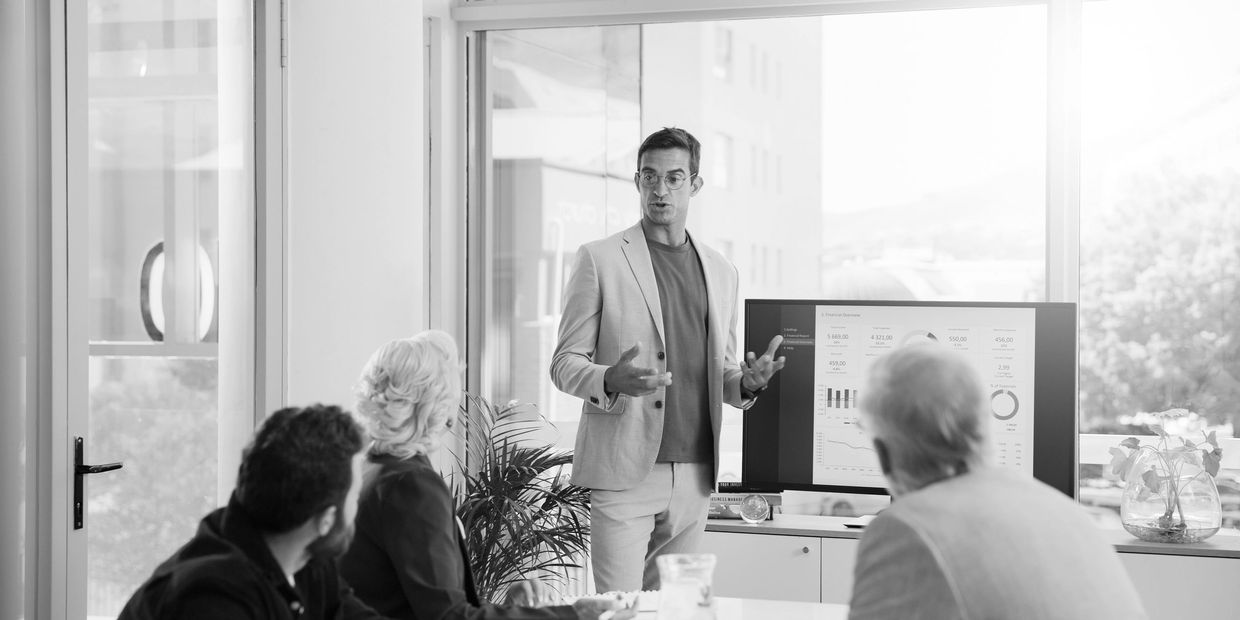 Man in beige suit presenting financial data to colleagues in a modern office.